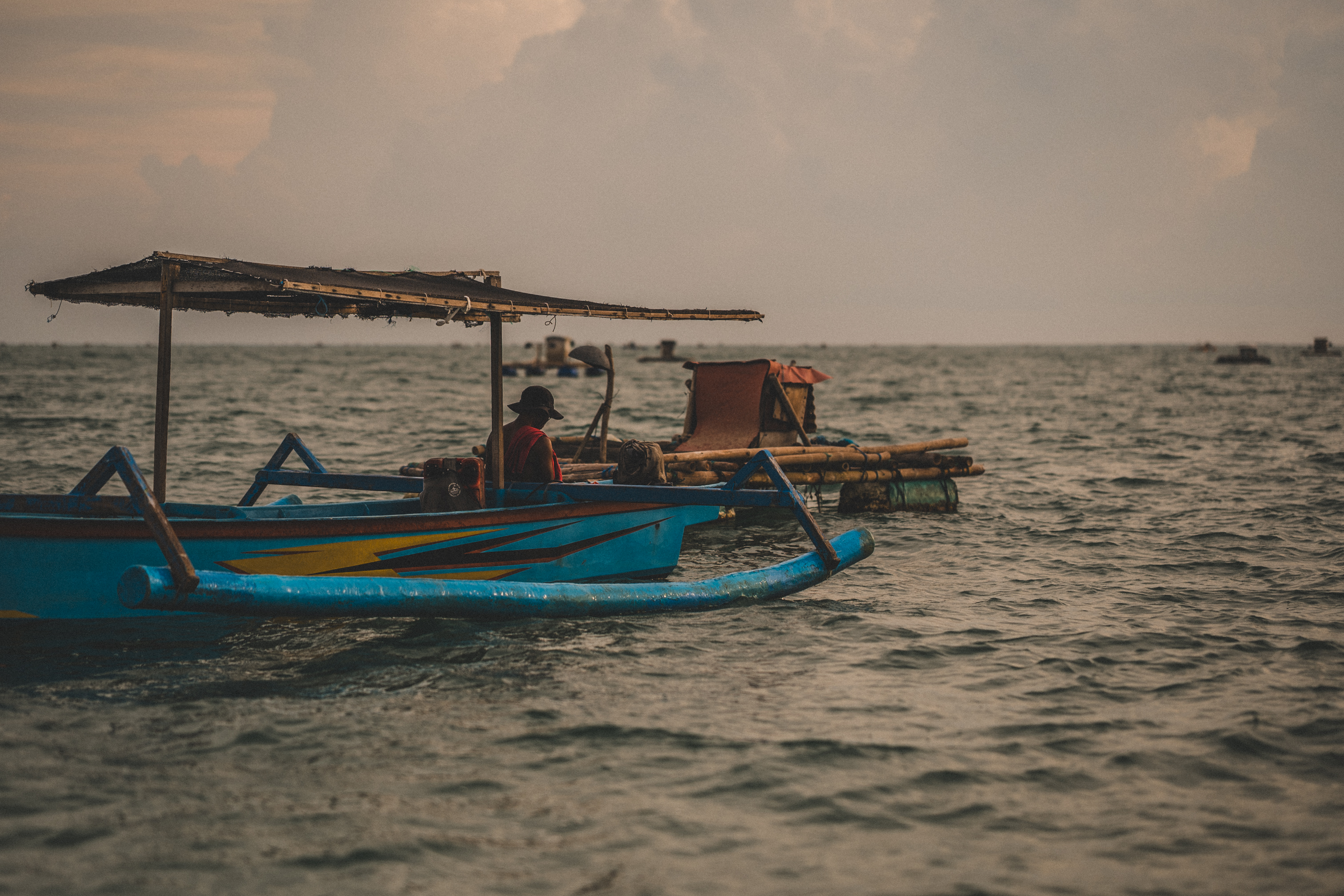 A blue outrigger fishing boat on the sea in warm evening light, Lombok