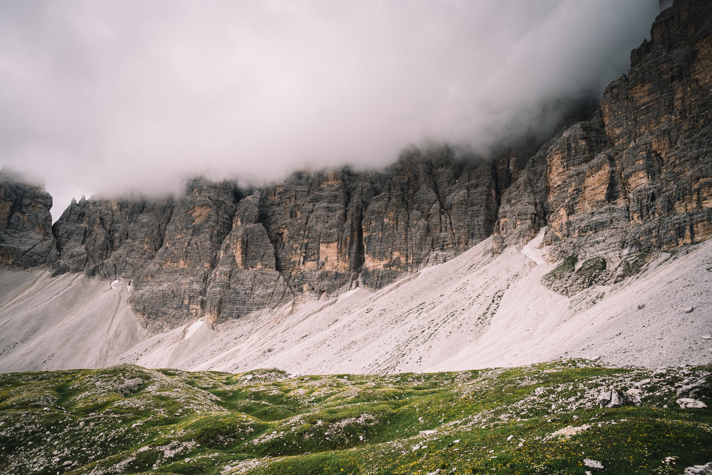 Tiefe Wolken über einer Felswand und grünen Bergwiesen