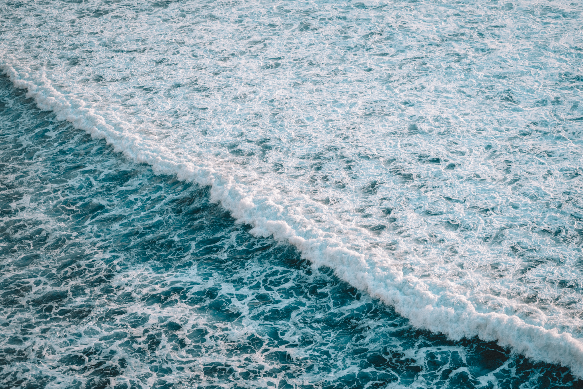 A wave breaking into turquoise sea foam from above