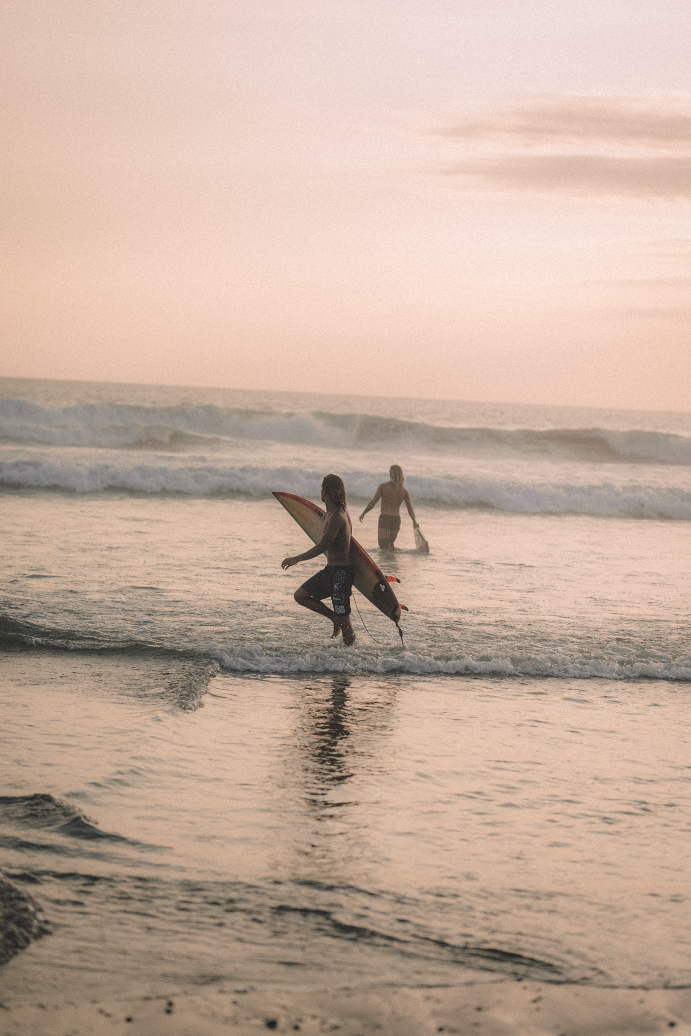Two surfers entering the water in soft evening light