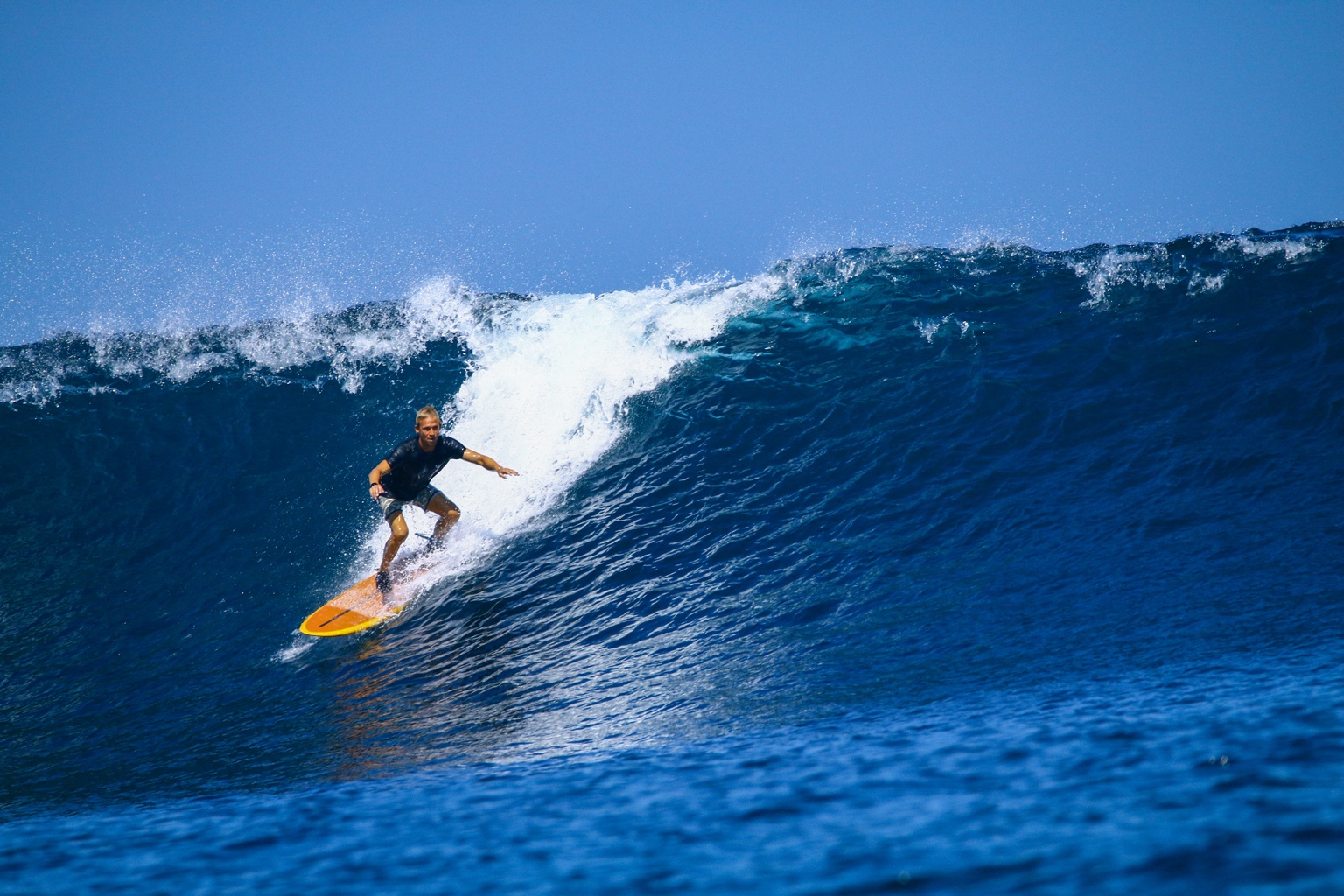 Harald Kuhm riding a blue wave on an orange surfboard in Indonesia