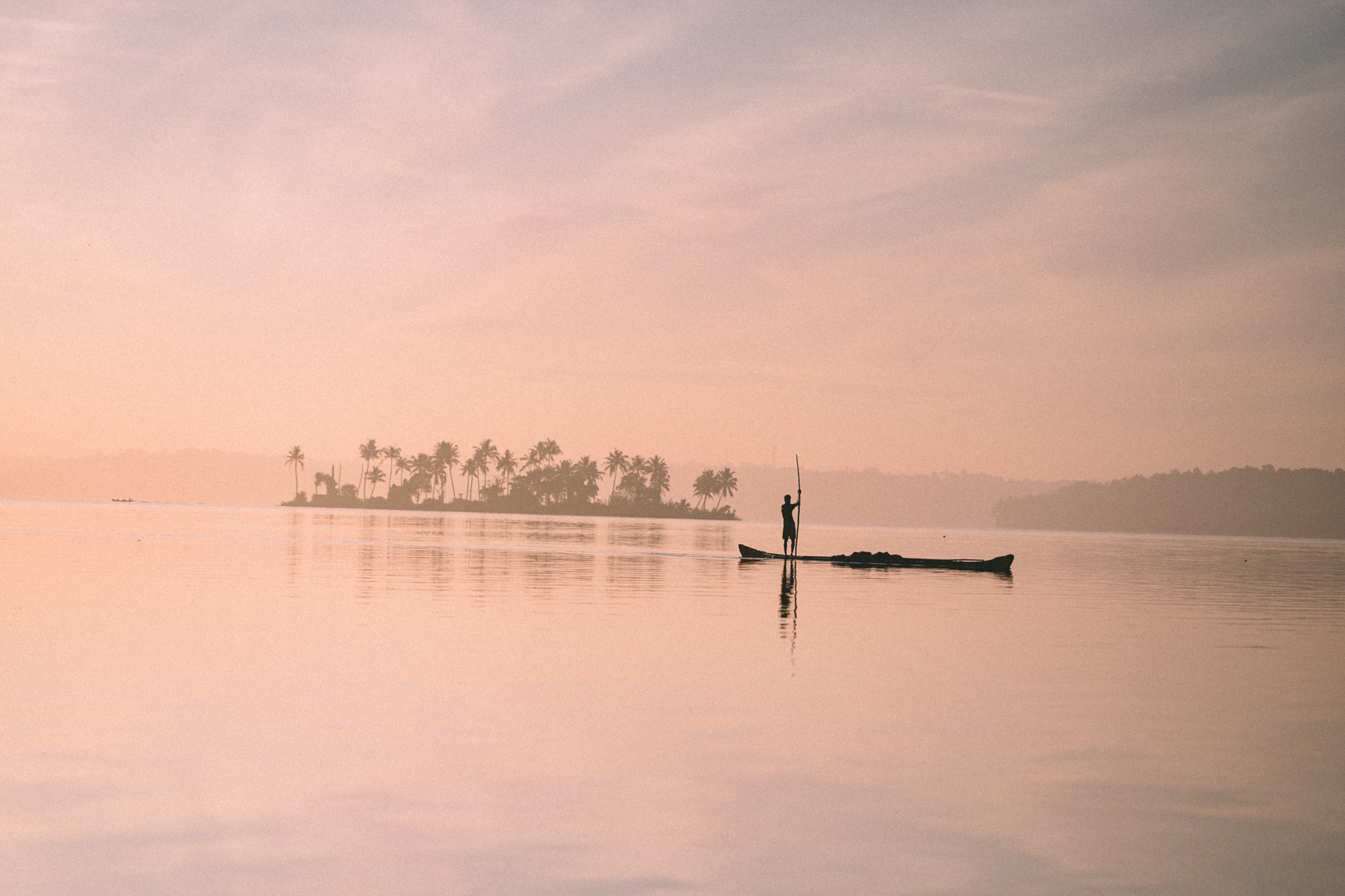 Ein Fischerboot vor einer Palmeninsel im Morgennebel