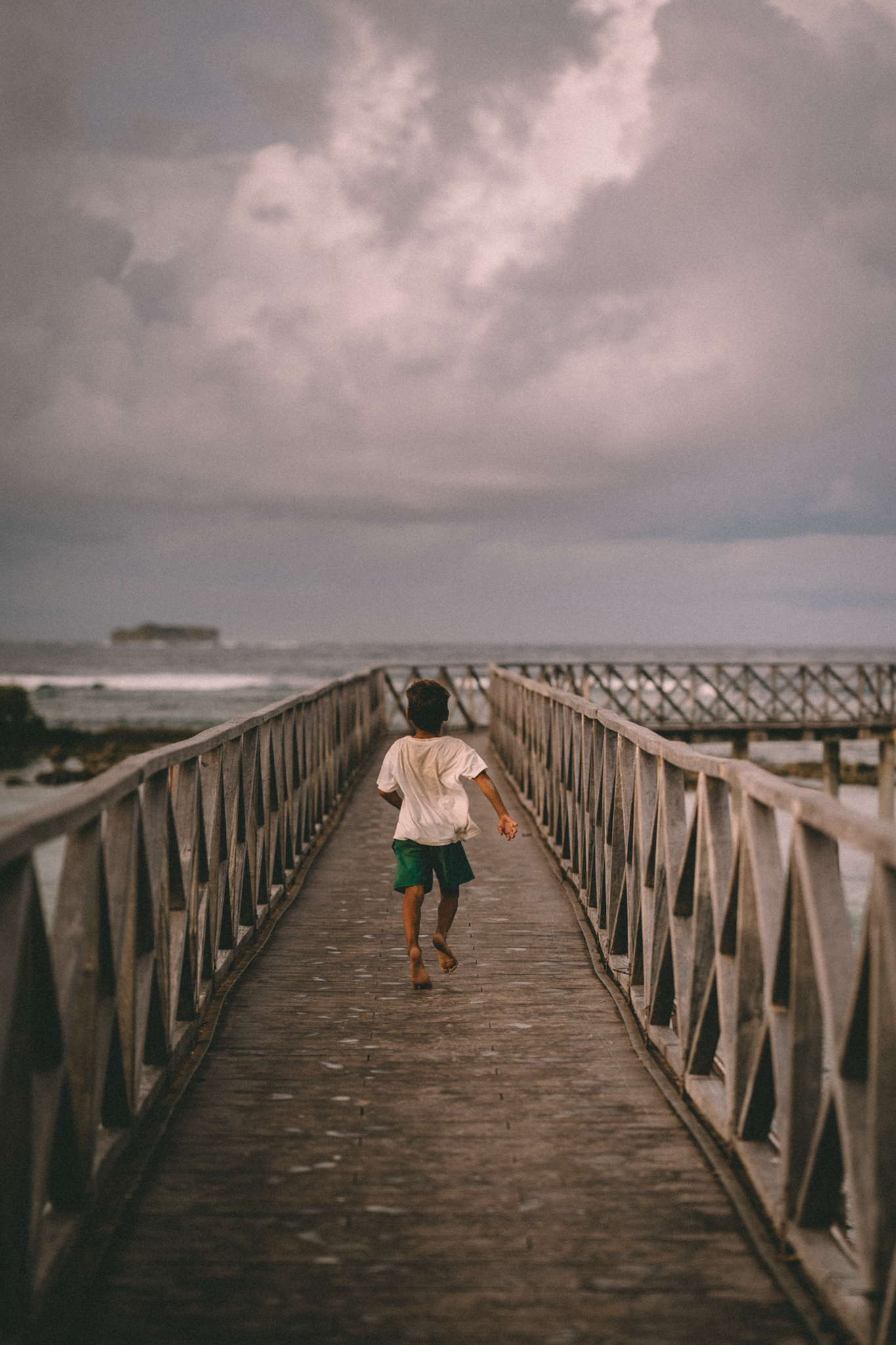 A child running along a wooden bridge to the sea