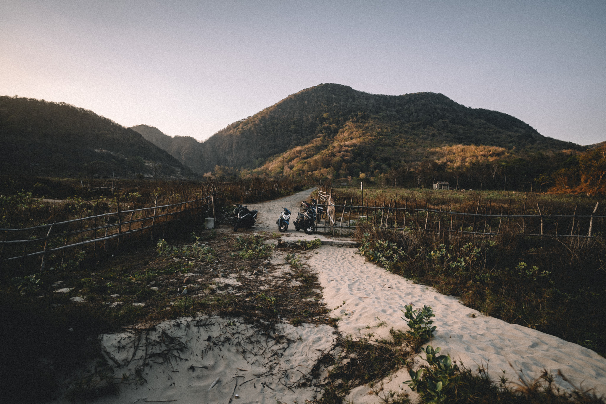 Scooters parked on a sandy track between hills in Sumbawa