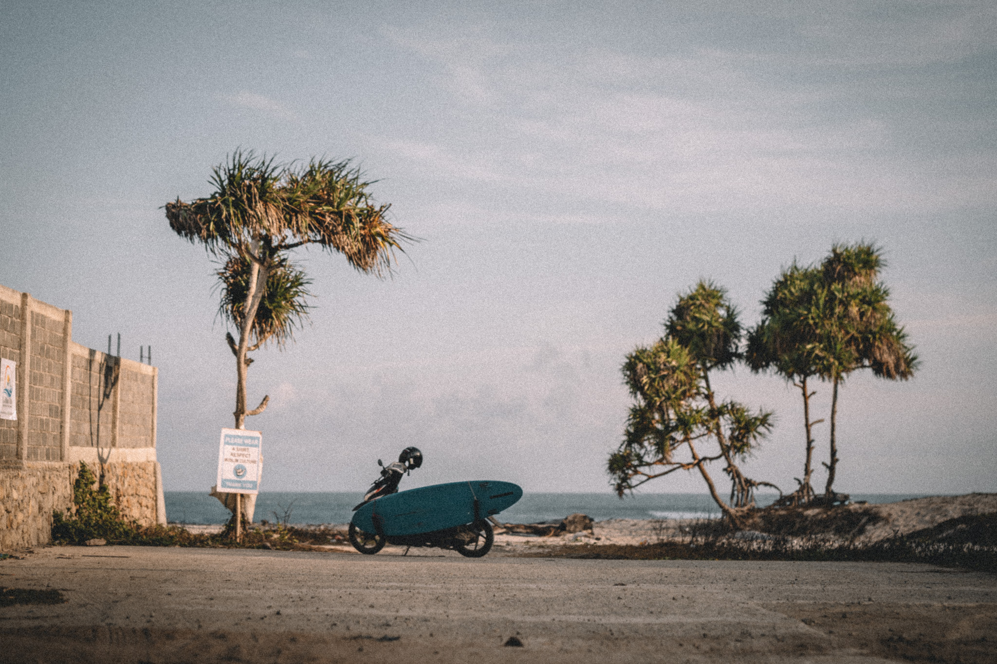 A scooter carrying a surfboard beside the coast