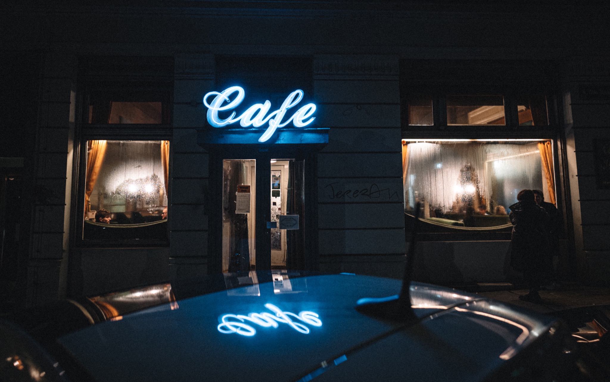 Blaues Café-Neonlicht spiegelt sich vor warm beleuchteten Fenstern