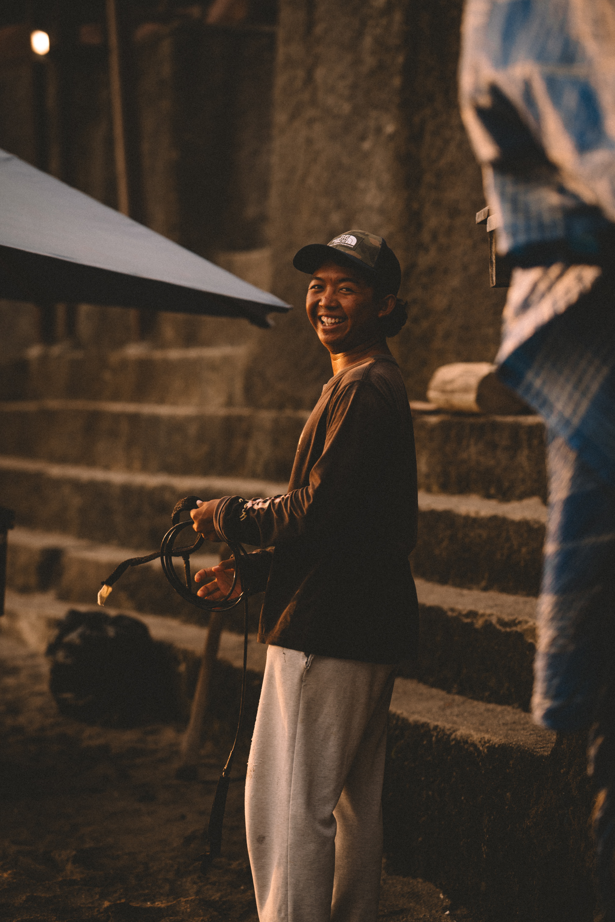 A smiling man holding a surfboard leash beside stone steps in Bali