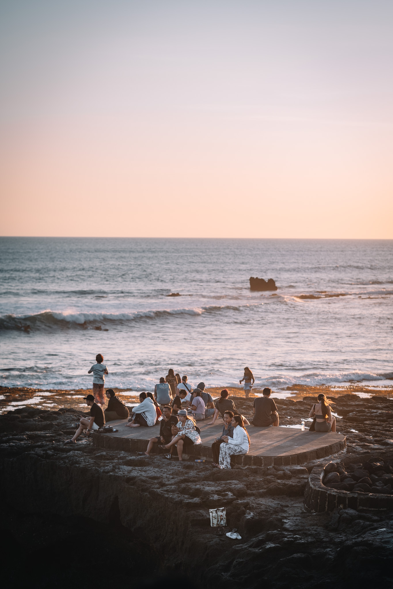 People gathering on a circular platform by the sea at sunset